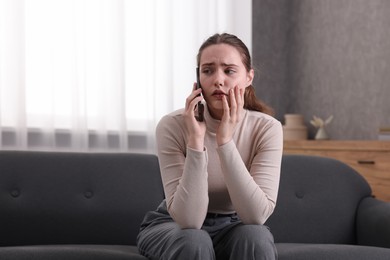 Photo of Depressed woman calling hotline for mental health help on sofa at home. Space for text