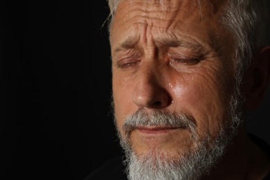 Photo of Sad senior man crying on black background, closeup. Space for text