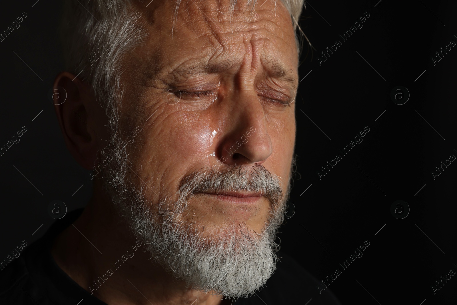 Photo of Sad senior man crying on black background, closeup. Space for text