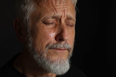 Photo of Sad senior man crying on black background, closeup. Space for text