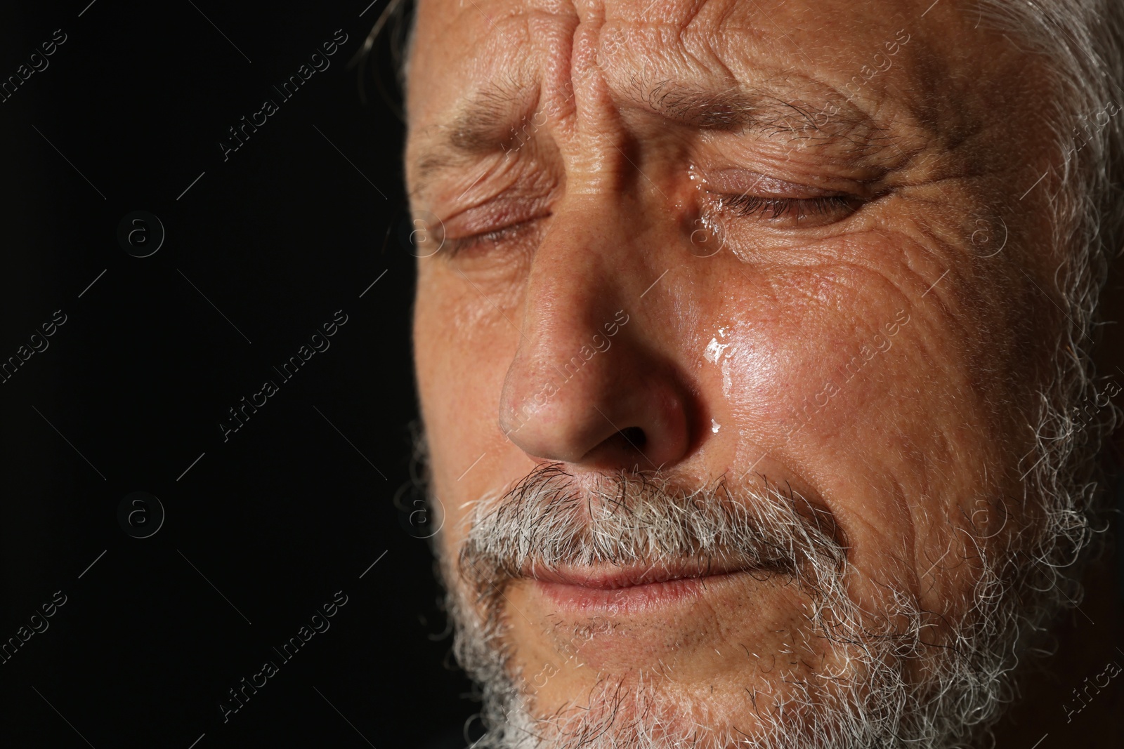 Photo of Sad senior man crying on black background, closeup