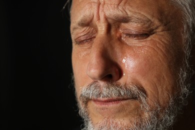 Photo of Sad senior man crying on black background, closeup