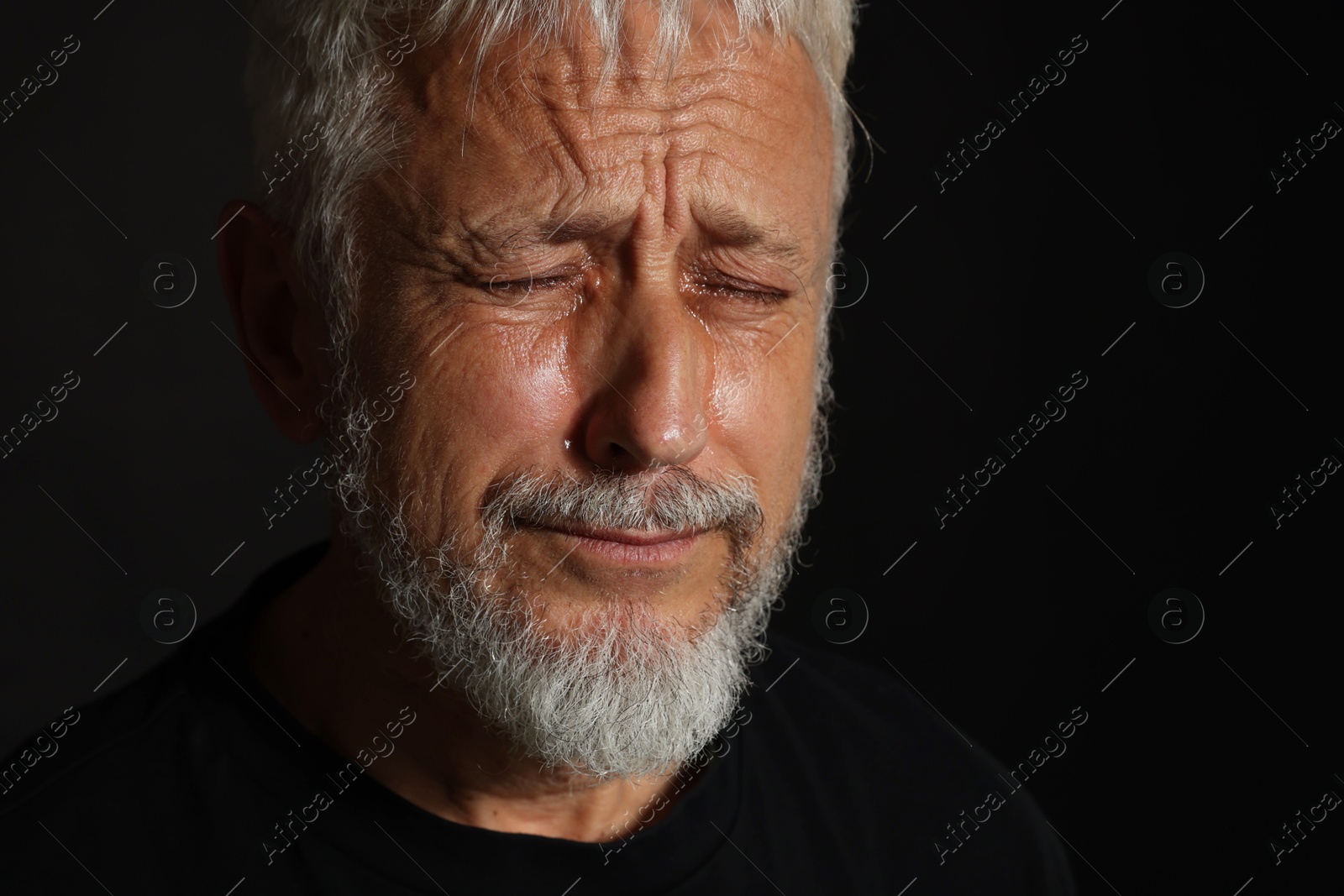 Photo of Sad senior man crying on black background, closeup. Space for text