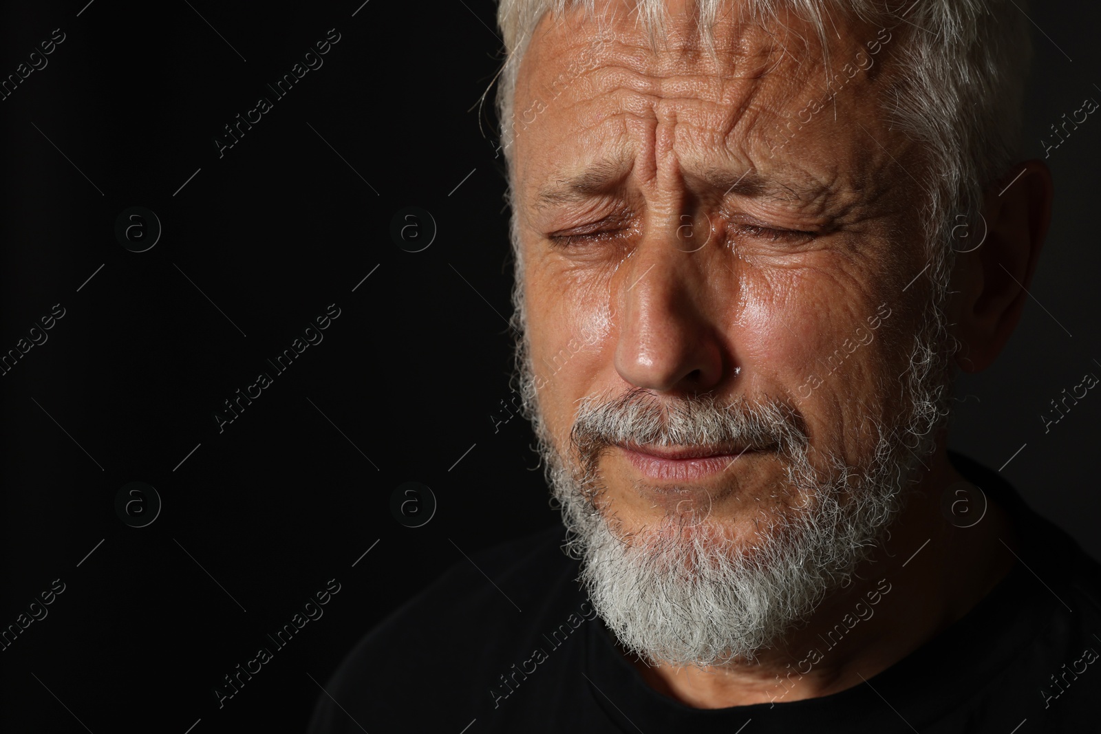 Photo of Sad senior man crying on black background, closeup. Space for text