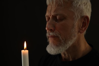 Photo of Sad senior man with burning candle crying on black background. Grieving loss