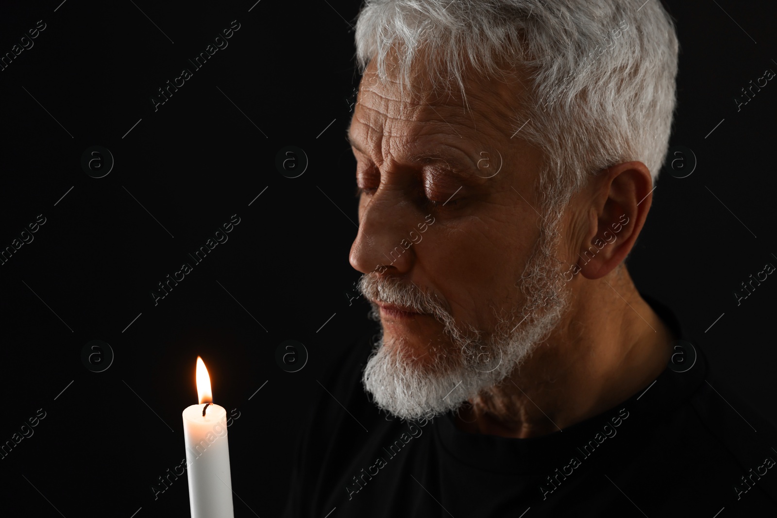 Photo of Sad senior man with burning candle crying on black background. Grieving loss