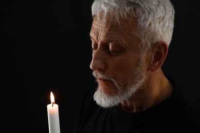 Photo of Sad senior man with burning candle crying on black background. Grieving loss