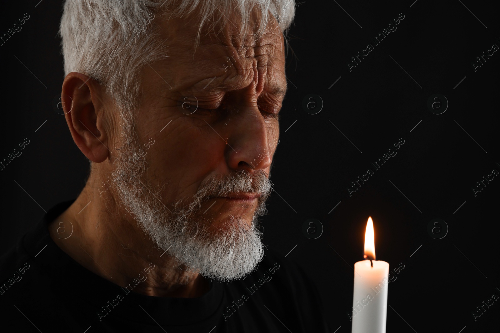 Photo of Sad senior man with burning candle crying on black background. Grieving loss