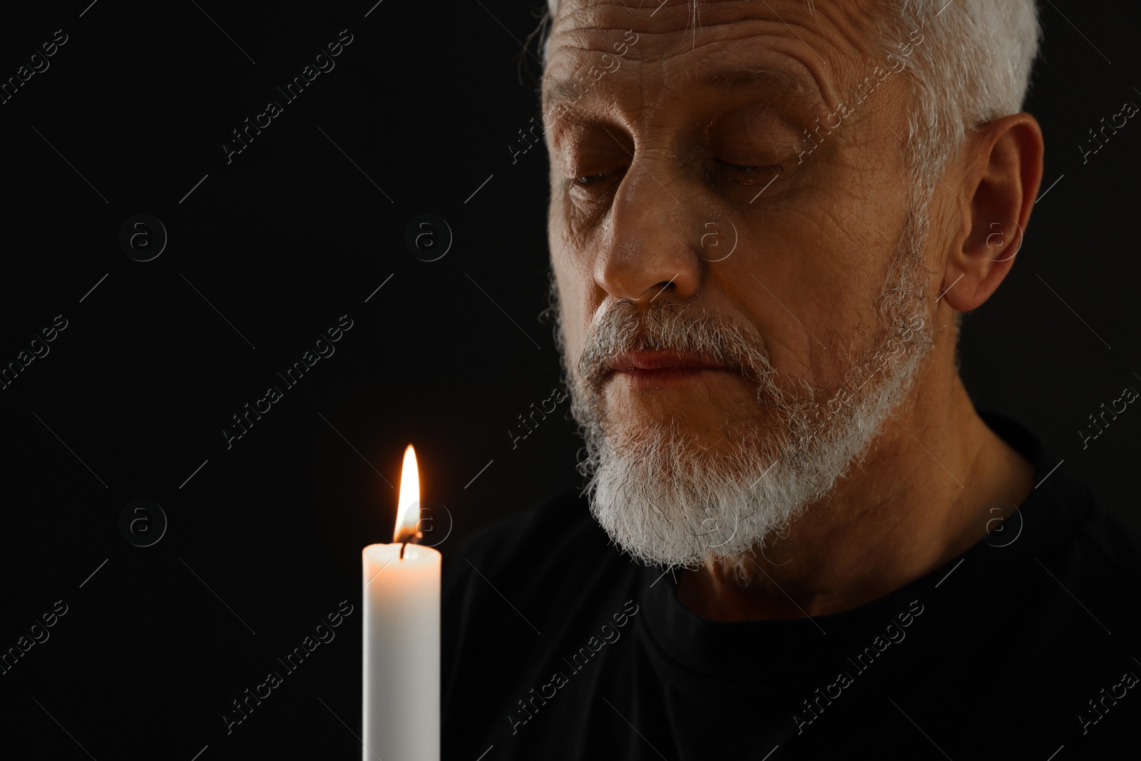 Photo of Sad senior man with burning candle crying on black background. Grieving loss