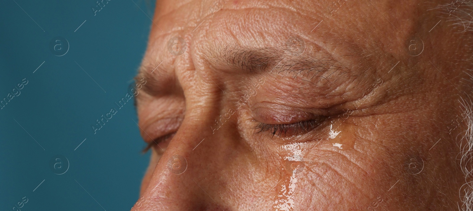 Photo of Sad senior man crying on blue background, closeup