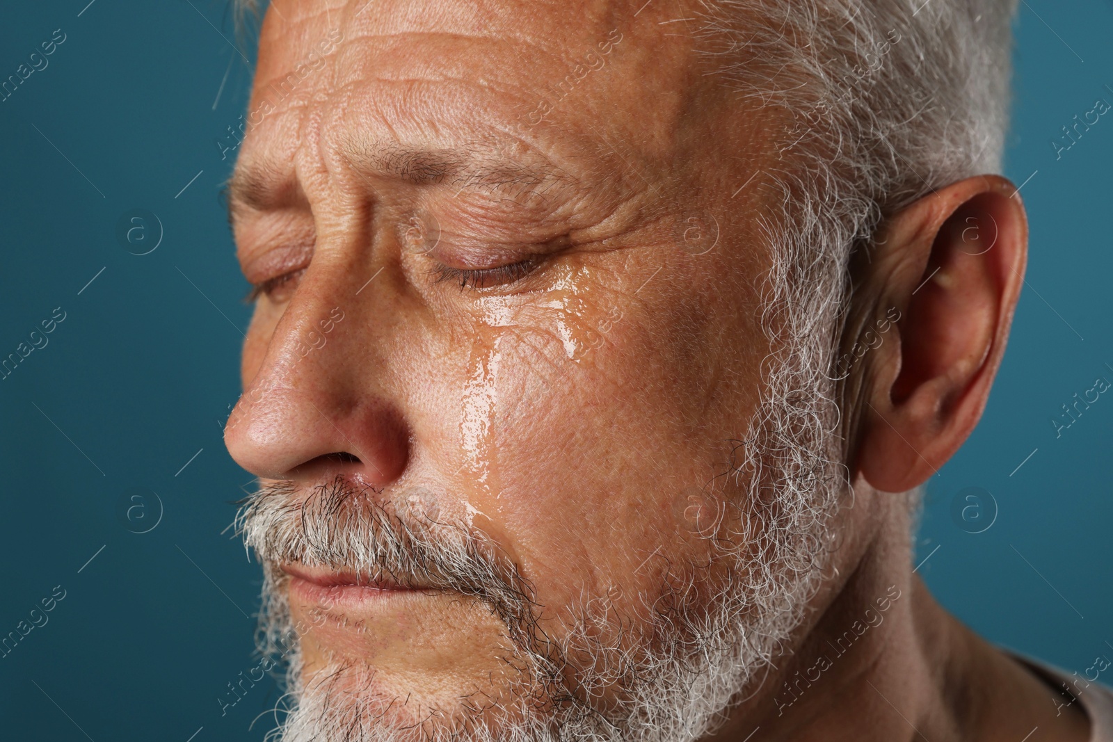 Photo of Sad senior man crying on blue background, closeup