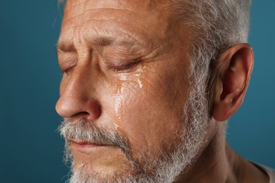 Photo of Sad senior man crying on blue background, closeup