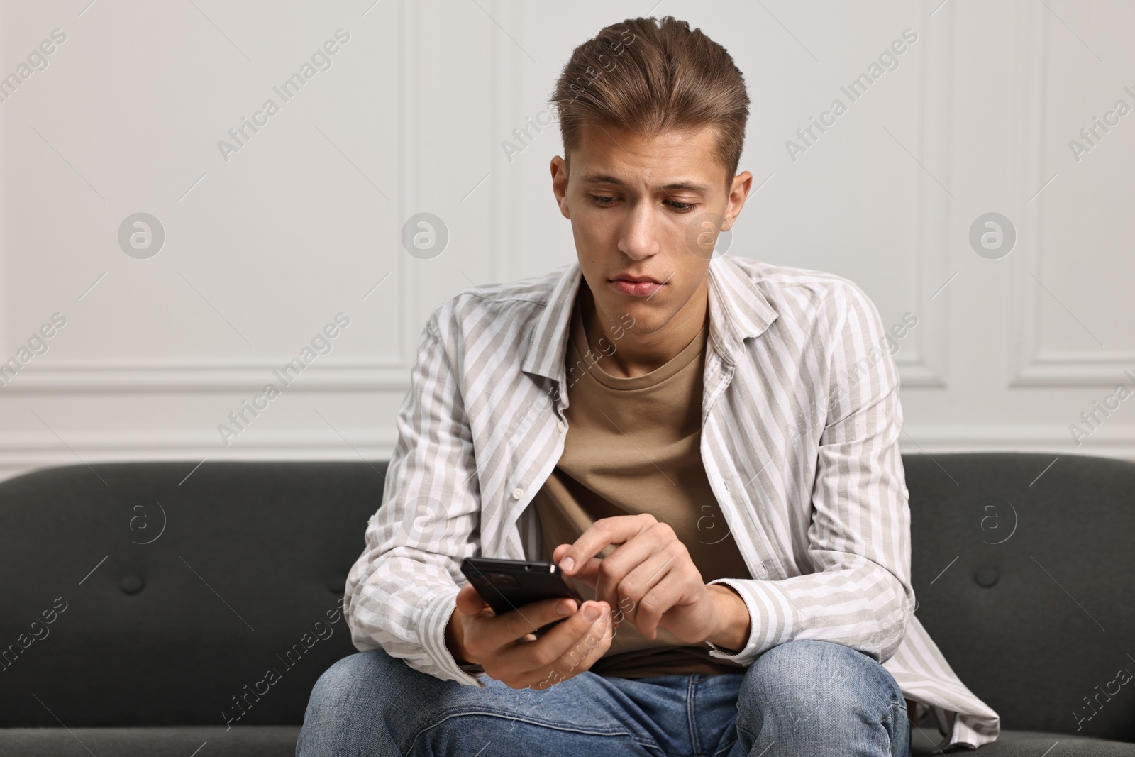 Photo of Stressed man calling hotline for mental health help on sofa at home