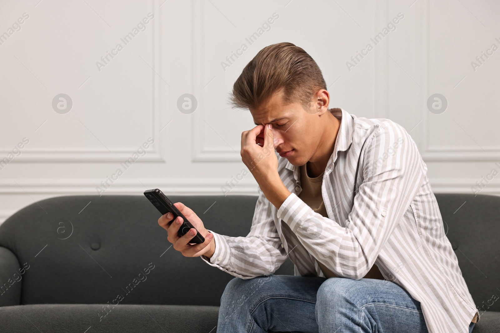 Photo of Stressed man calling hotline for mental health help on sofa at home. Space for text