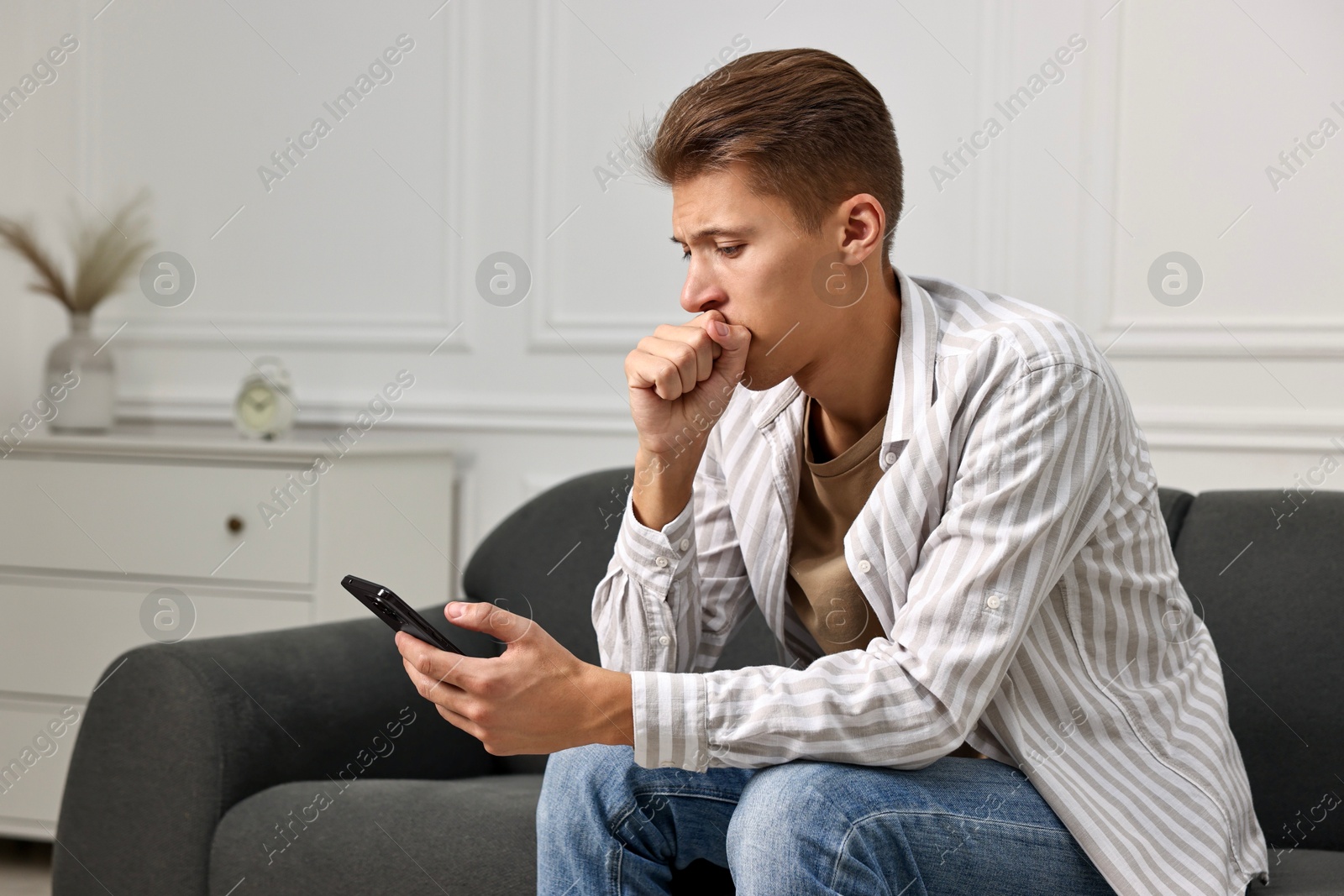 Photo of Worried man calling hotline for mental health help on sofa at home. Space for text