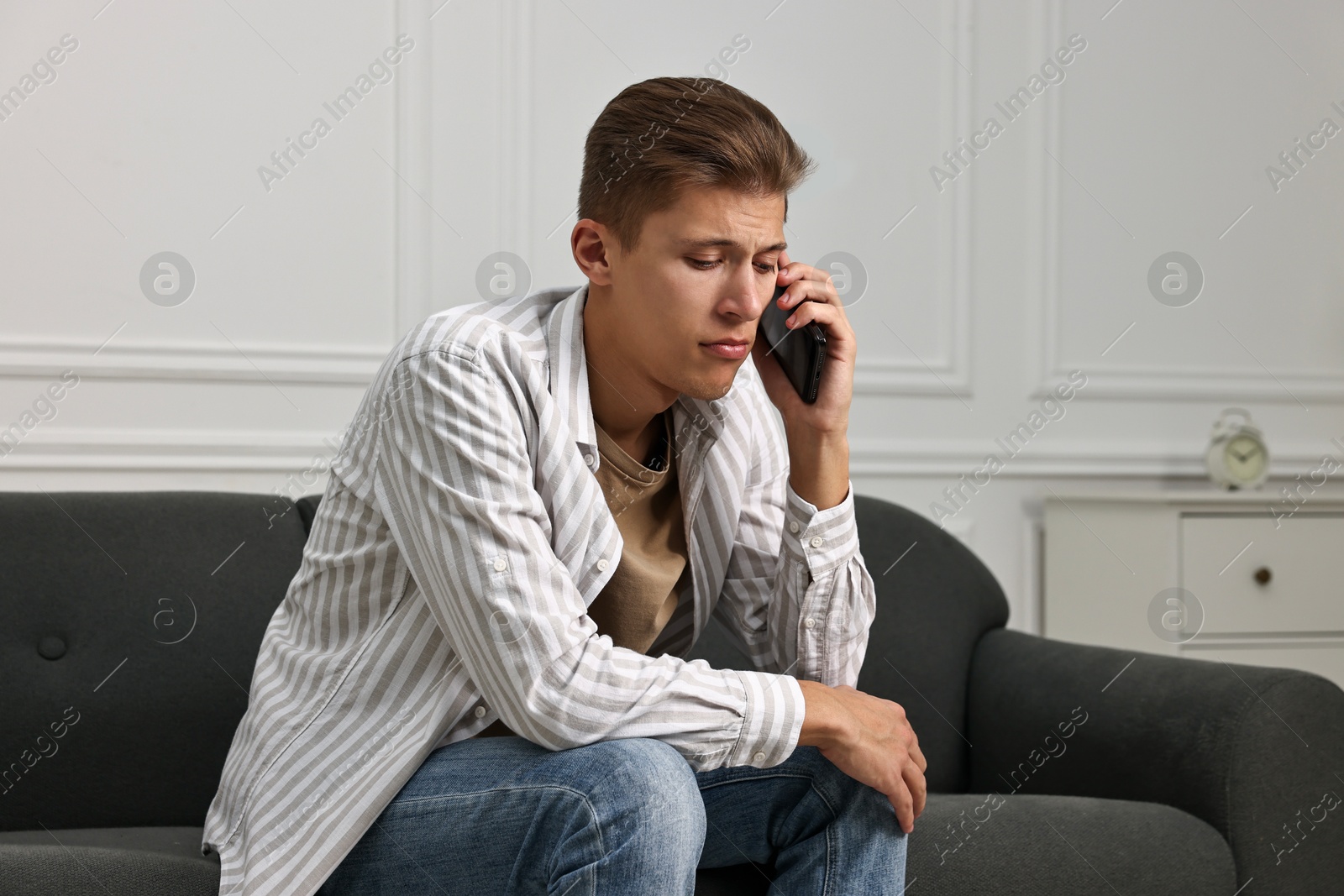 Photo of Stressed man calling hotline for mental health help on sofa at home