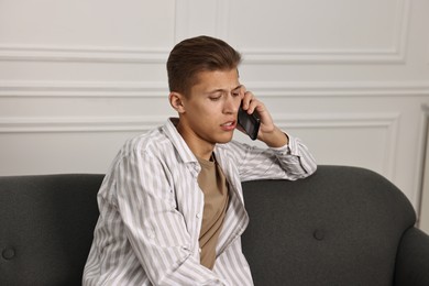 Photo of Stressed man calling hotline for mental health help on sofa at home