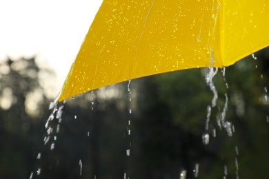 Photo of Open yellow umbrella under pouring rain outdoors, closeup