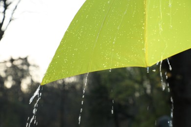 Photo of Open yellow umbrella under pouring rain outdoors, closeup