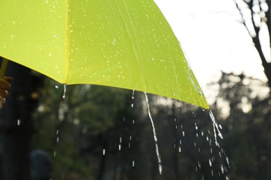 Photo of Open yellow umbrella under pouring rain outdoors, closeup