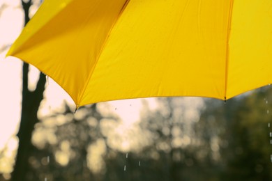 Photo of Open yellow umbrella under pouring rain outdoors, closeup