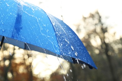 Photo of Open blue umbrella under pouring rain outdoors, closeup