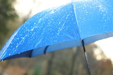 Photo of Open blue umbrella under pouring rain outdoors, closeup