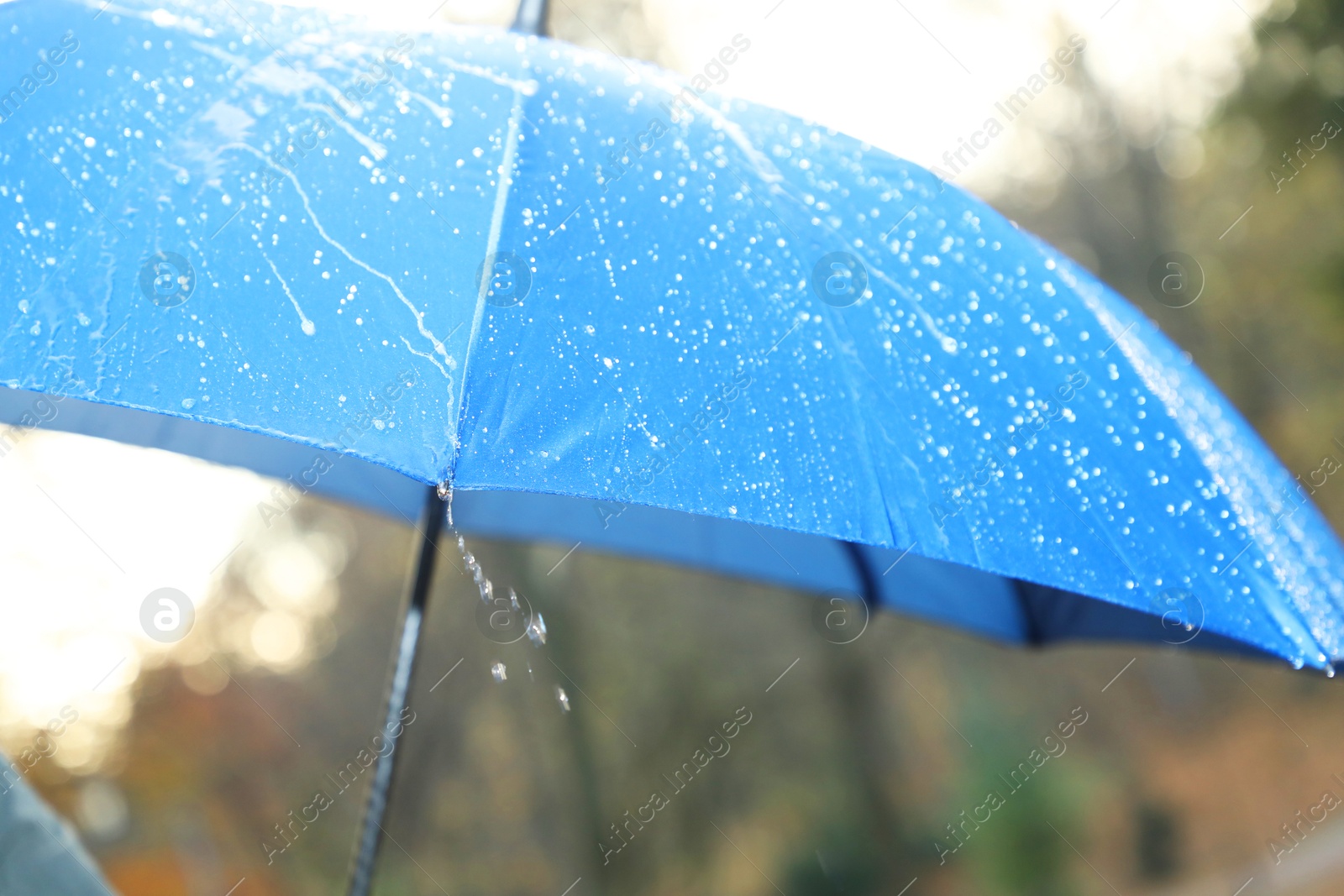 Photo of Open blue umbrella under pouring rain outdoors, closeup