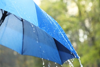 Photo of Open blue umbrella under pouring rain outdoors, closeup. Space for text