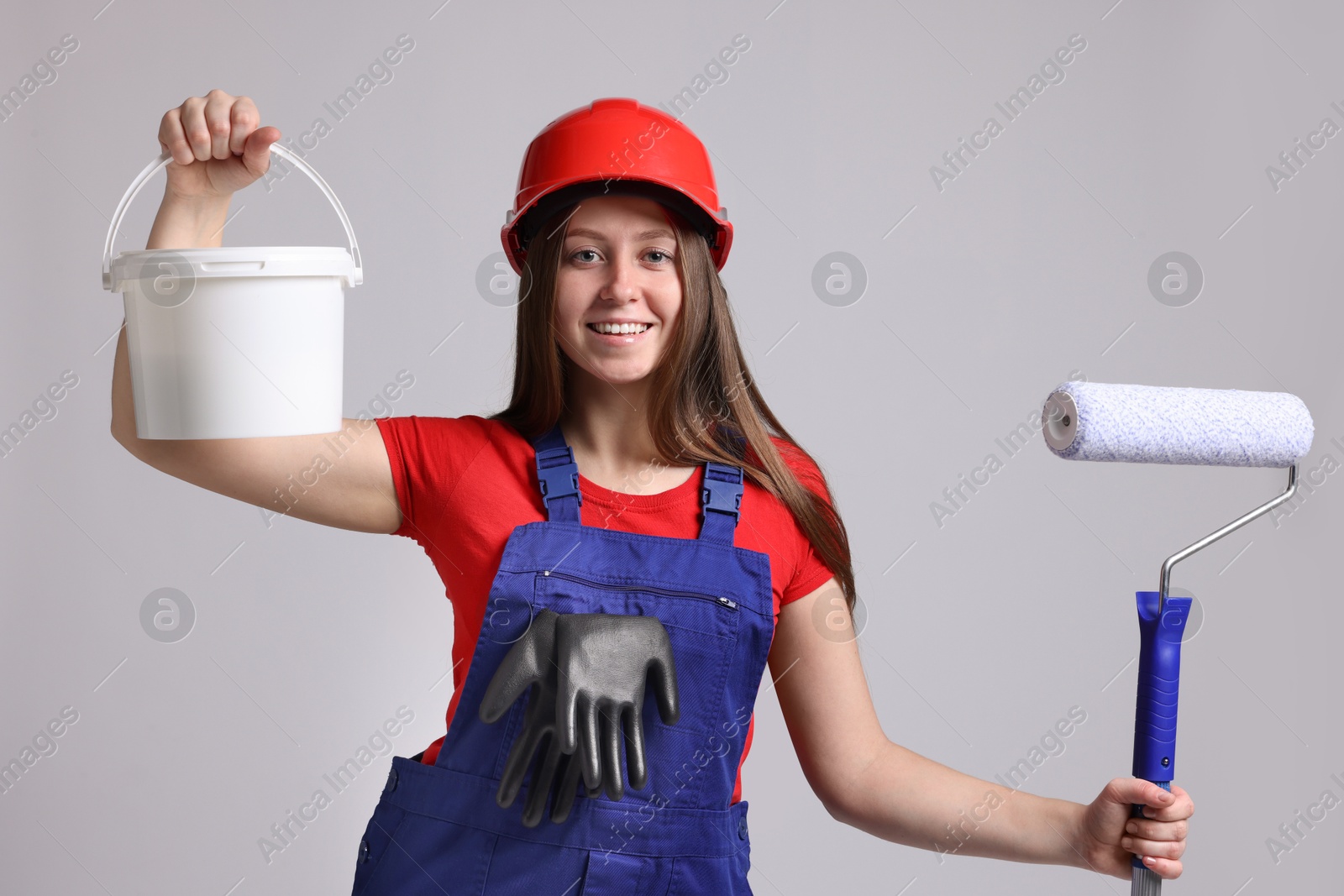 Photo of Professional painter with roller and bucket of paint on light grey background