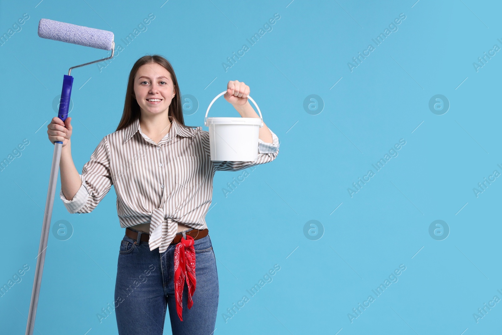 Photo of Woman with roller and bucket of paint on light blue background. Space for text