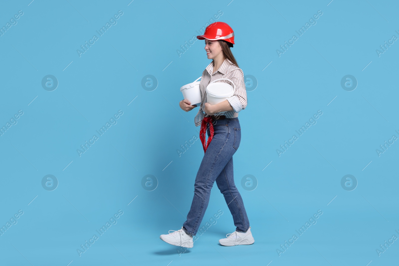 Photo of Woman wearing hardhat with buckets of paint on light blue background