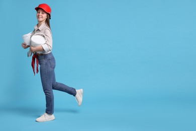 Photo of Woman wearing hardhat with buckets of paint on light blue background. Space for text