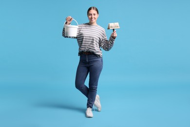 Photo of Woman with brush and bucket of paint on light blue background