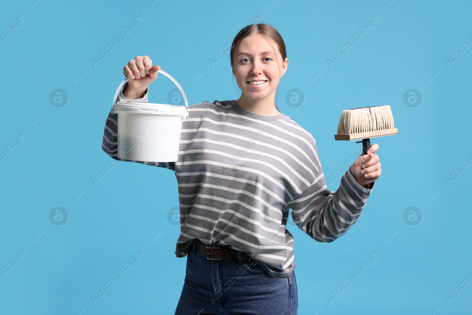 Photo of Woman with brush and bucket of paint on light blue background