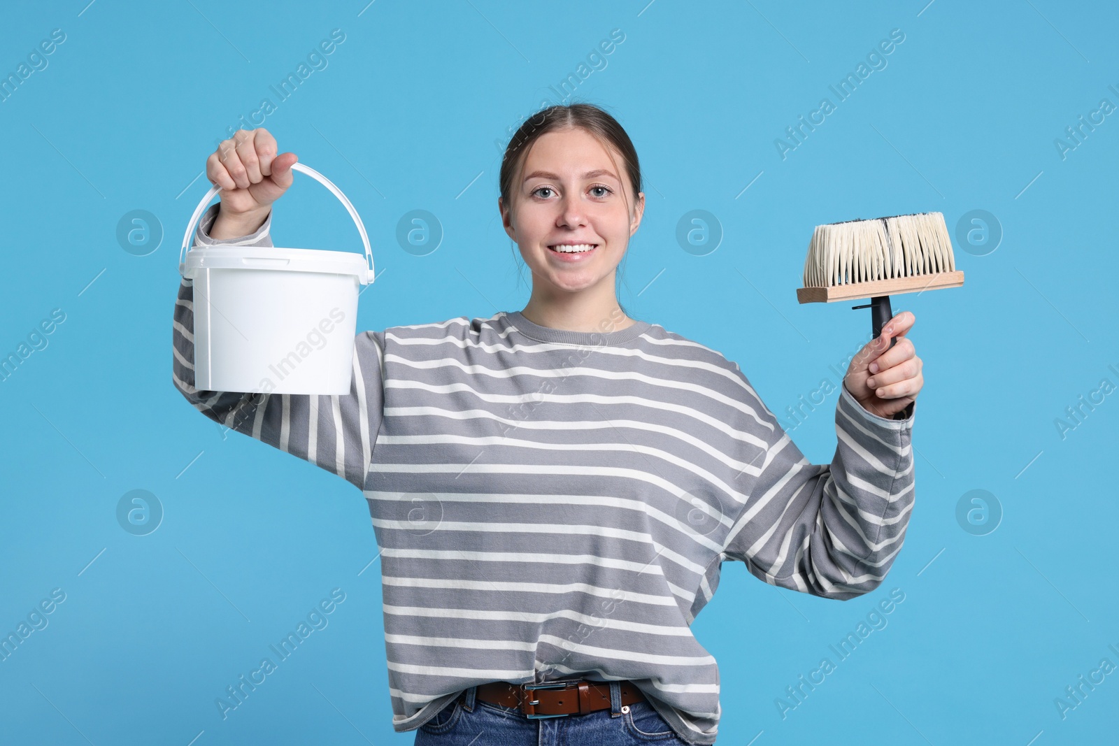 Photo of Woman with brush and bucket of paint on light blue background