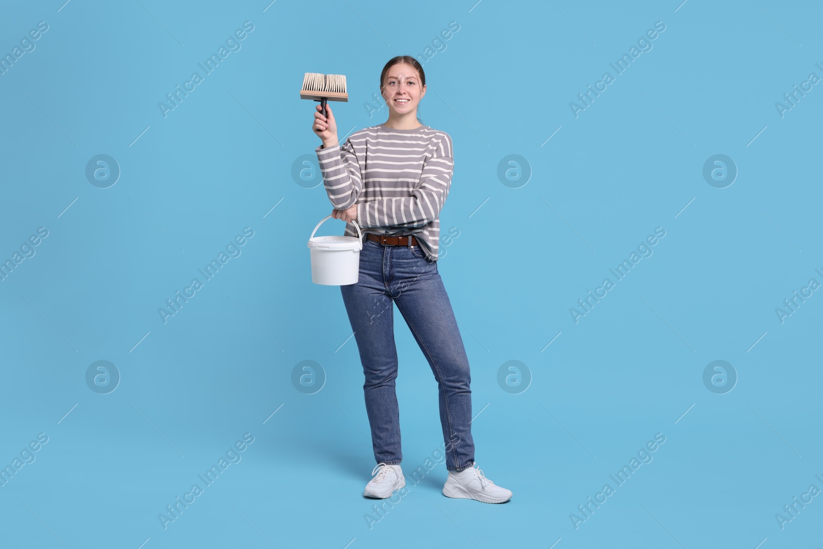 Photo of Woman with brush and bucket of paint on light blue background