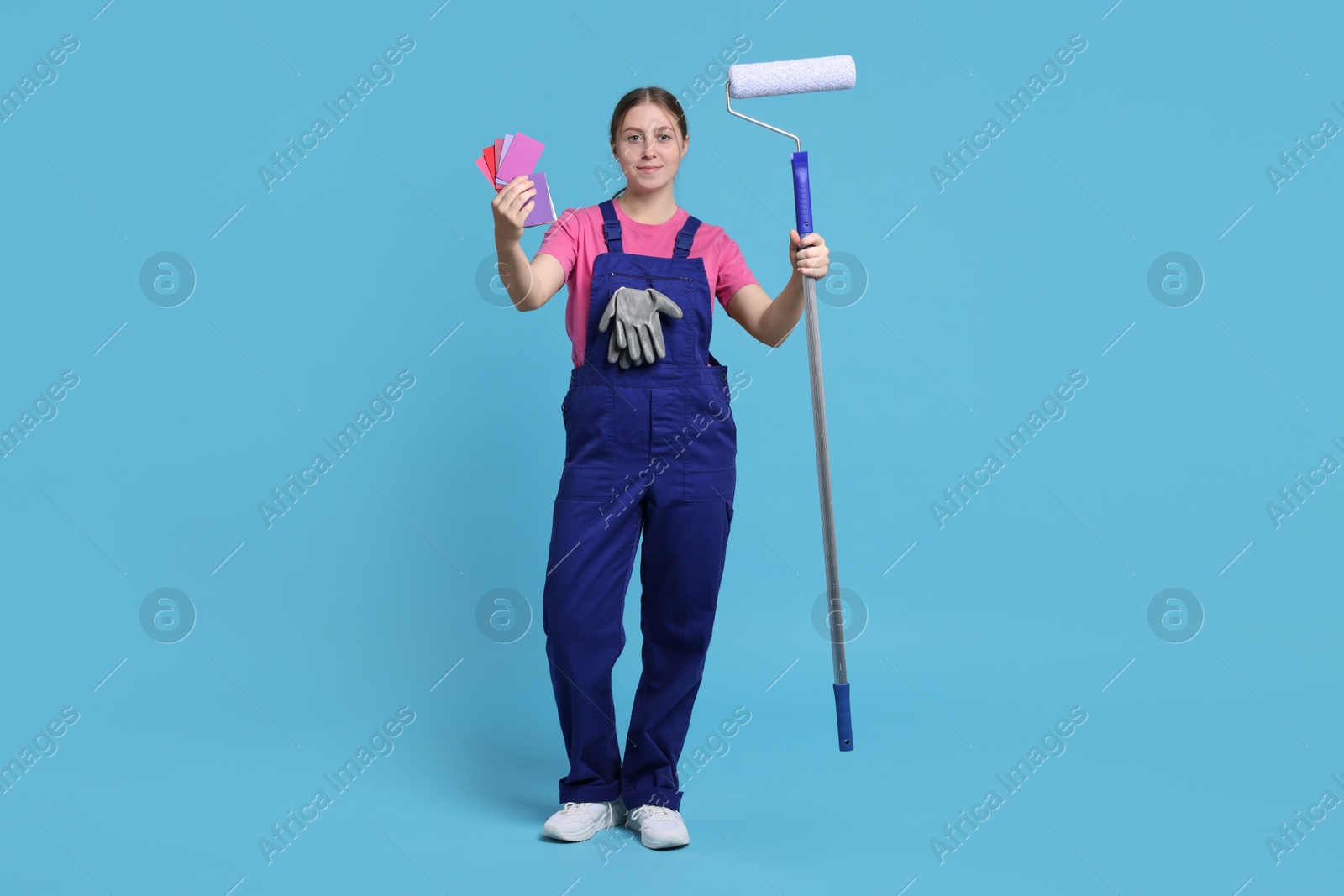 Photo of Professional painter with roller and color samples on light blue background