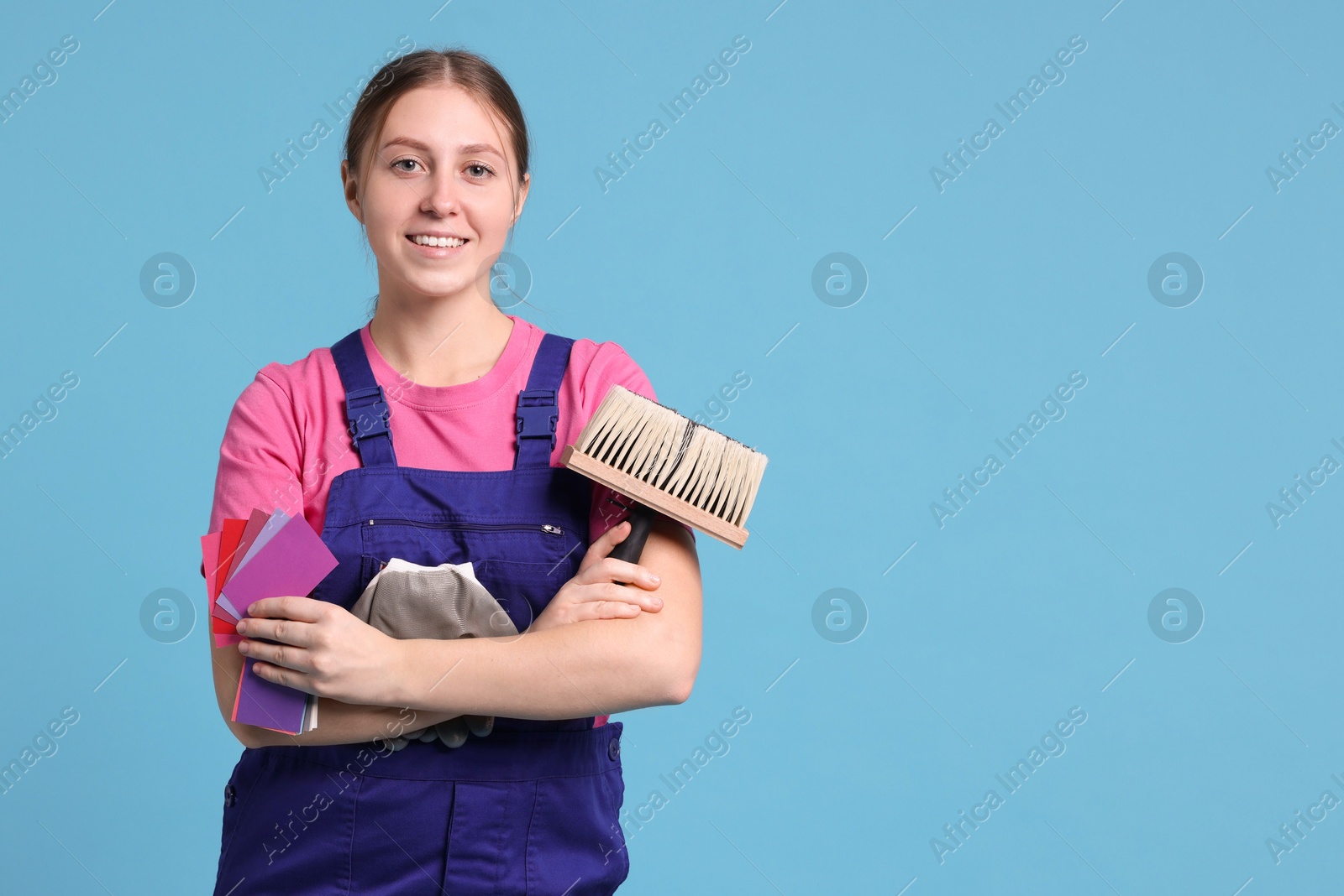 Photo of Professional painter with brush and color samples on light blue background. Space for text