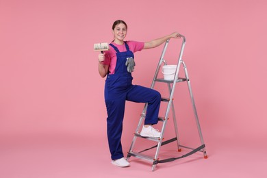 Photo of Professional painter with brush, bucket of paint and ladder on light pink background