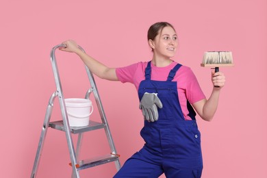 Photo of Professional painter with brush, bucket of paint and ladder on light pink background