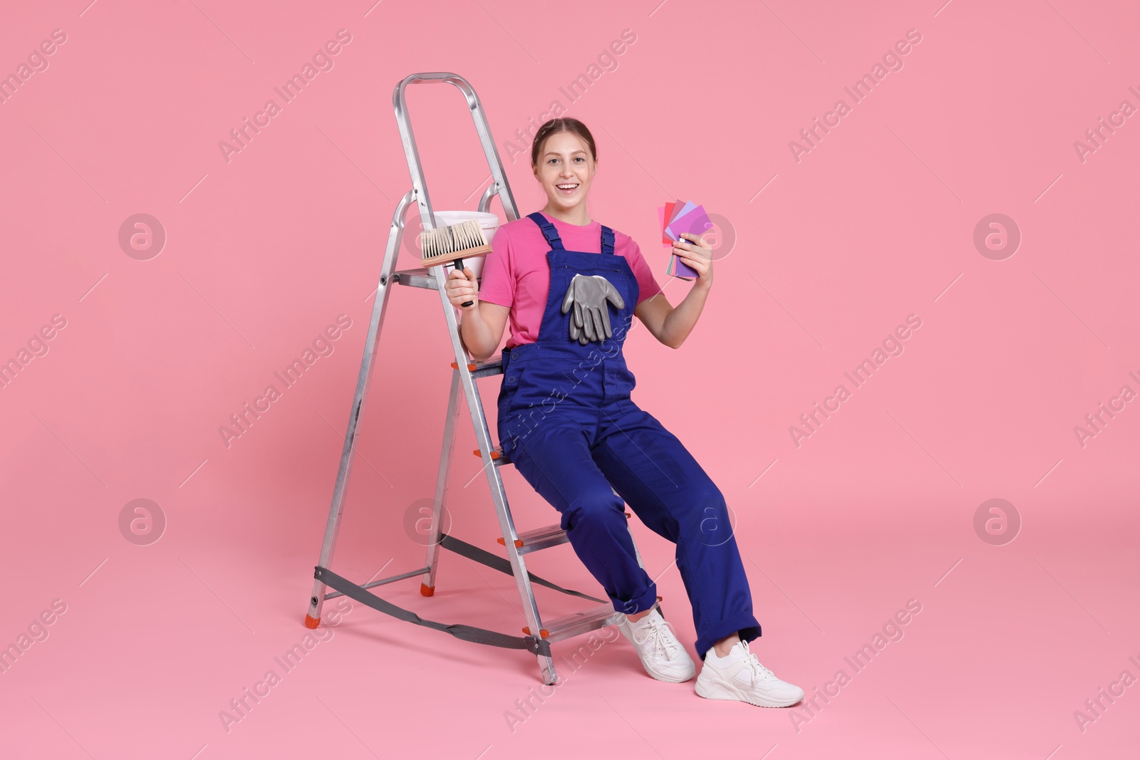 Photo of Professional painter with brush, color samples and ladder on light pink background