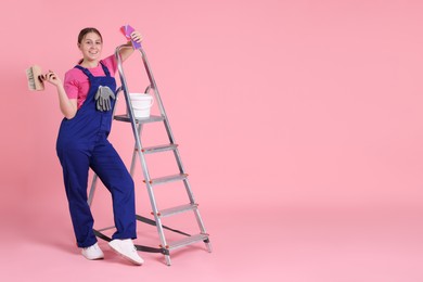 Photo of Professional painter with brush, color samples, bucket of paint and ladder on light pink background. Space for text