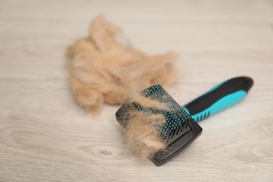 Photo of Grooming brush and pile of pet's hair on wooden floor, closeup