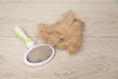 Photo of Grooming brush and pile of pet's hair on wooden floor