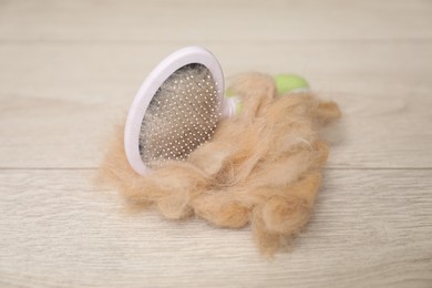 Photo of Grooming brush and pile of pet's hair on wooden floor, closeup