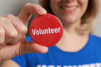 Photo of Woman holding button badge with word Volunteer on grey background, closeup