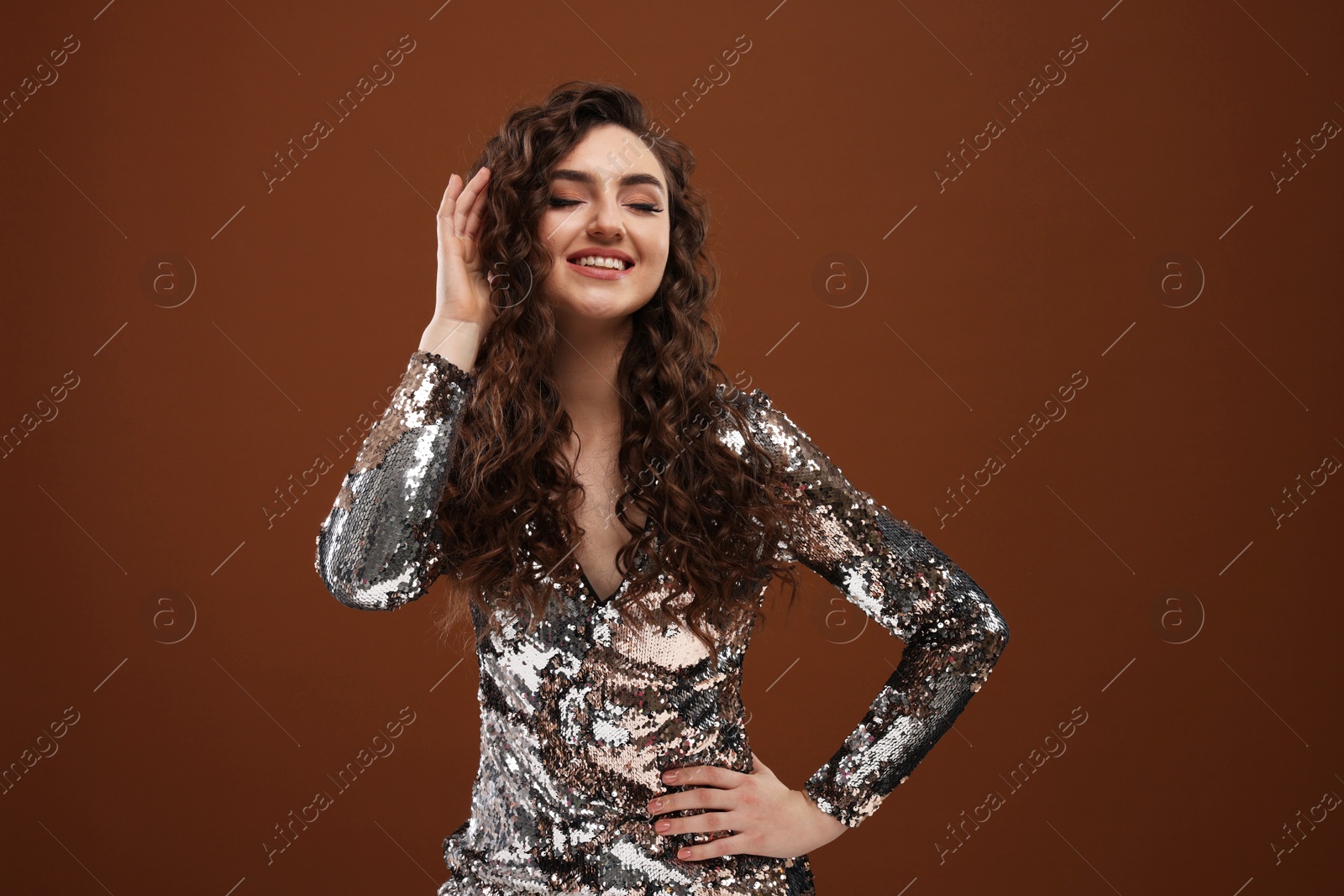 Photo of Beautiful young woman with long curly hair in sequin dress on brown background