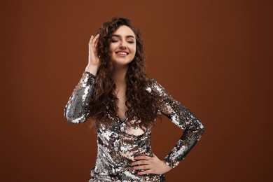 Photo of Beautiful young woman with long curly hair in sequin dress on brown background