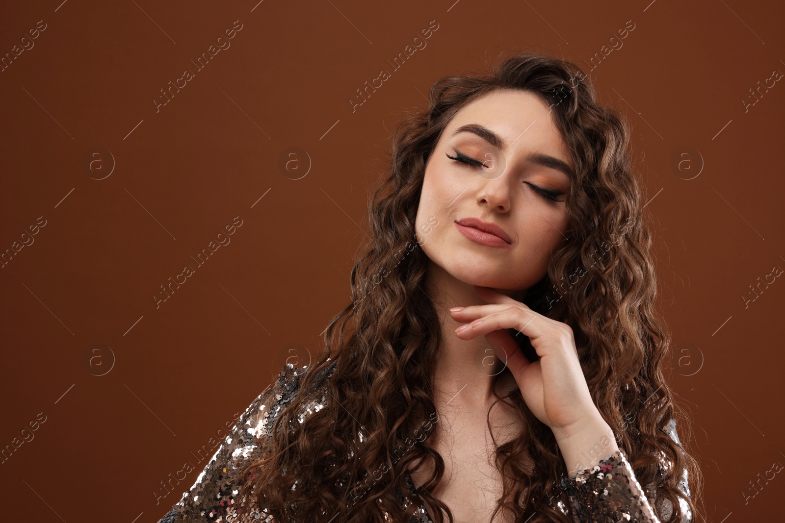 Photo of Beautiful young woman with long curly hair in sequin dress on brown background, space for text